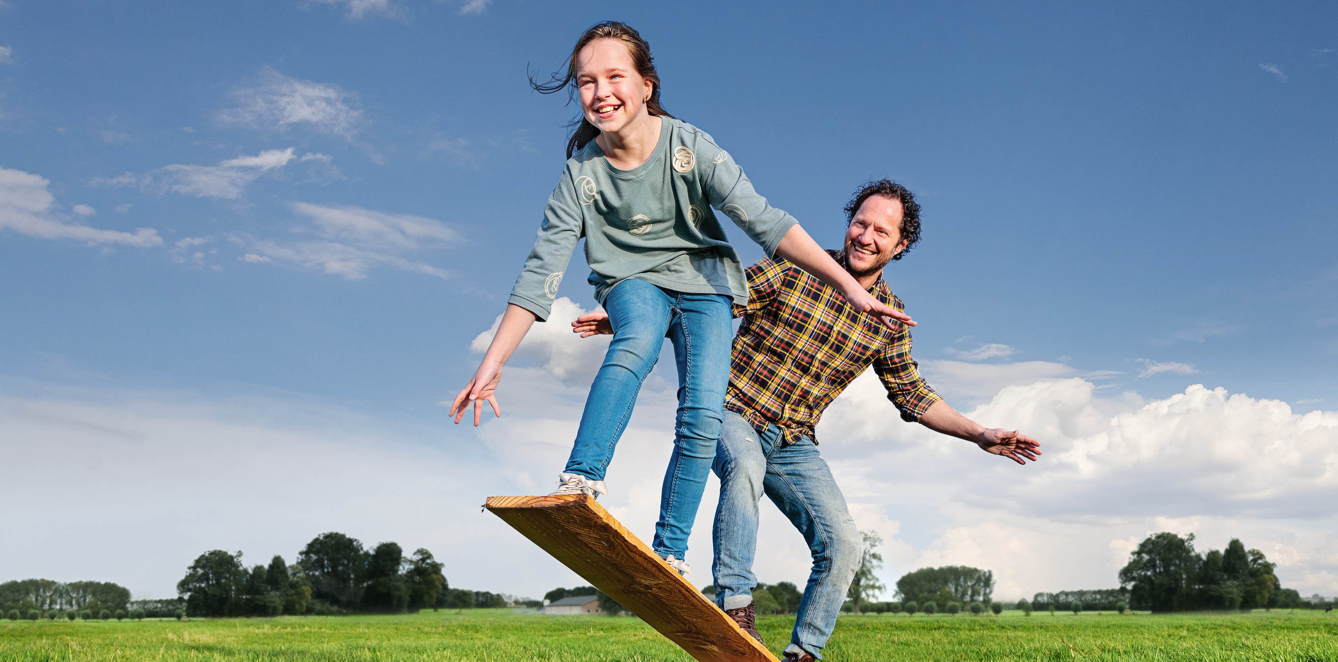 A man and a child jumping on a wooden board in a field.
